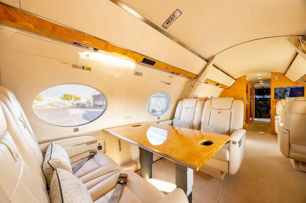Cabine do Gulfstream G650ER com poltronas de couro claro, mesa de trabalho em madeira e janelas ovais.